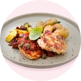 Gebackene Hähnchenschenkel mit kleinen Kartoffeln, Speckbohnen und einer Basilikumblätter-Dekoration auf einem grauen Teller.