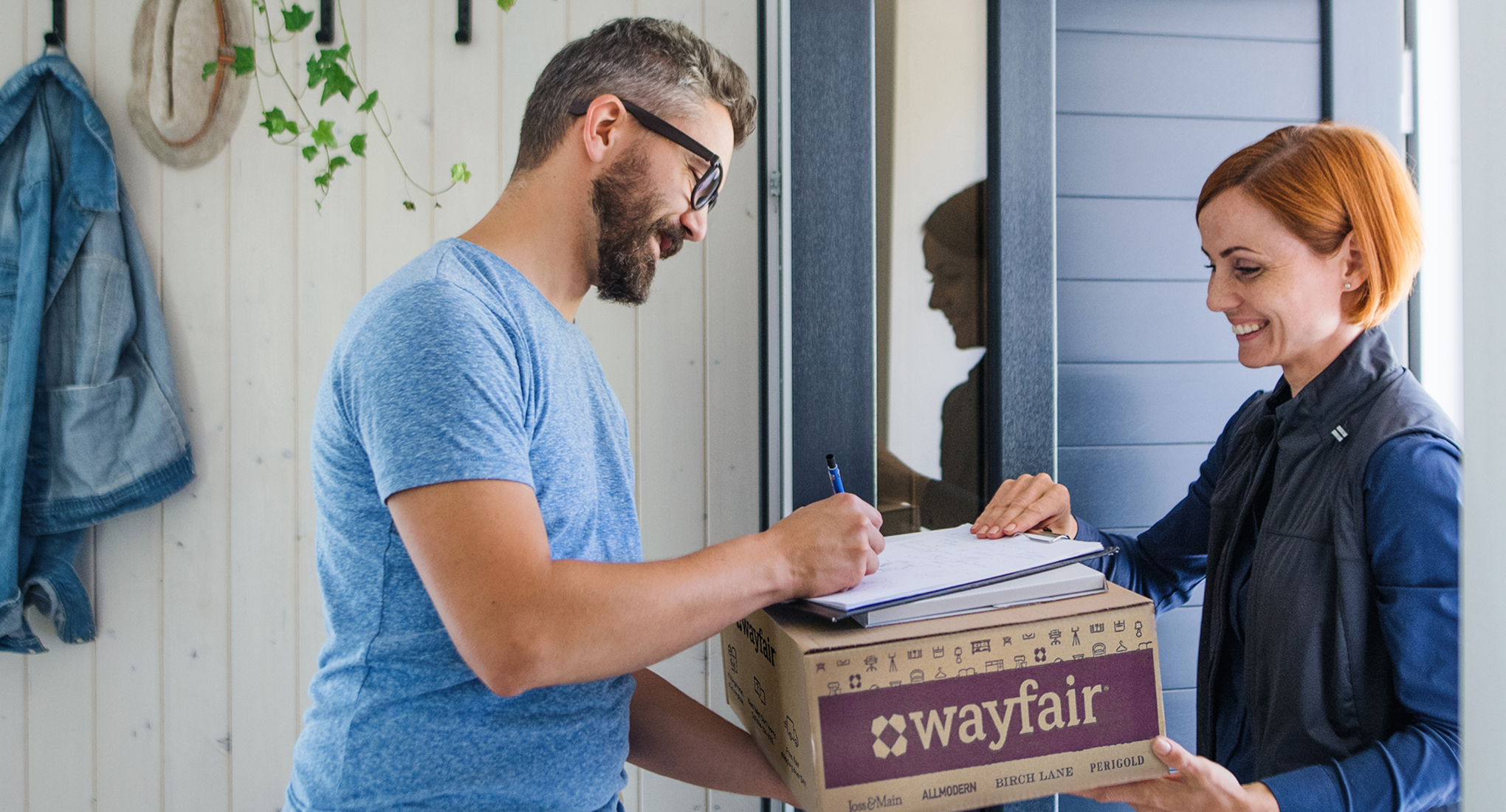 A woman delivering a Wayfair package to a man signing for it