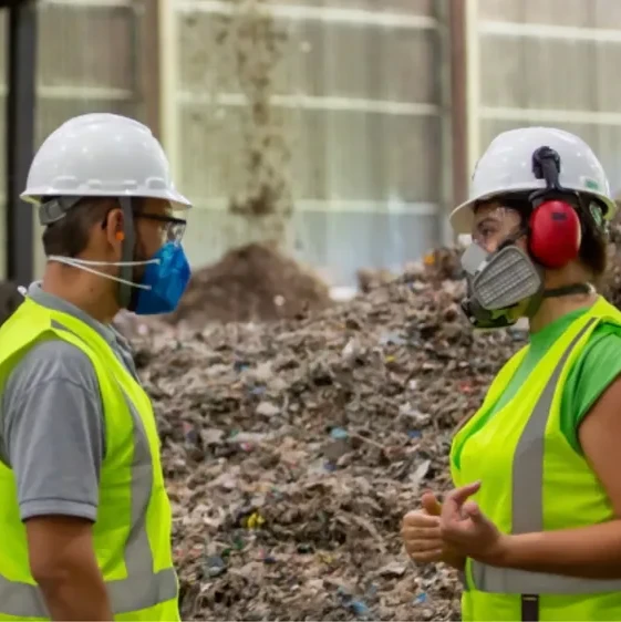Two people in hardhats and wearing respiratory masks talking